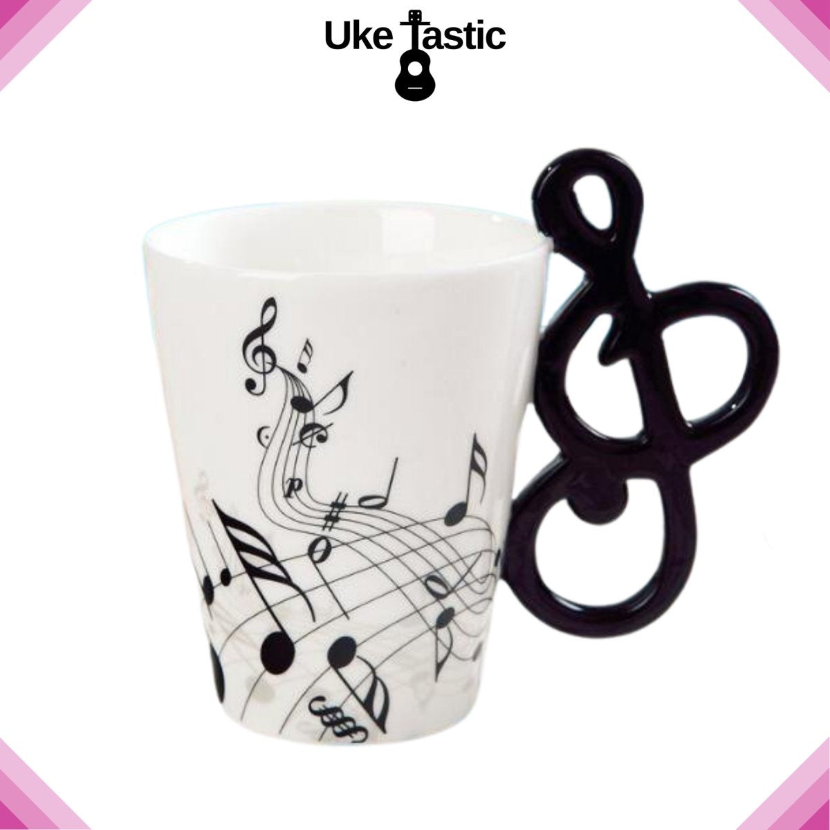 A white ceramic mug with a music-themed design, featuring notes and a handle shaped like a uke, displayed against a white background with the text 'UKE TASIC'.